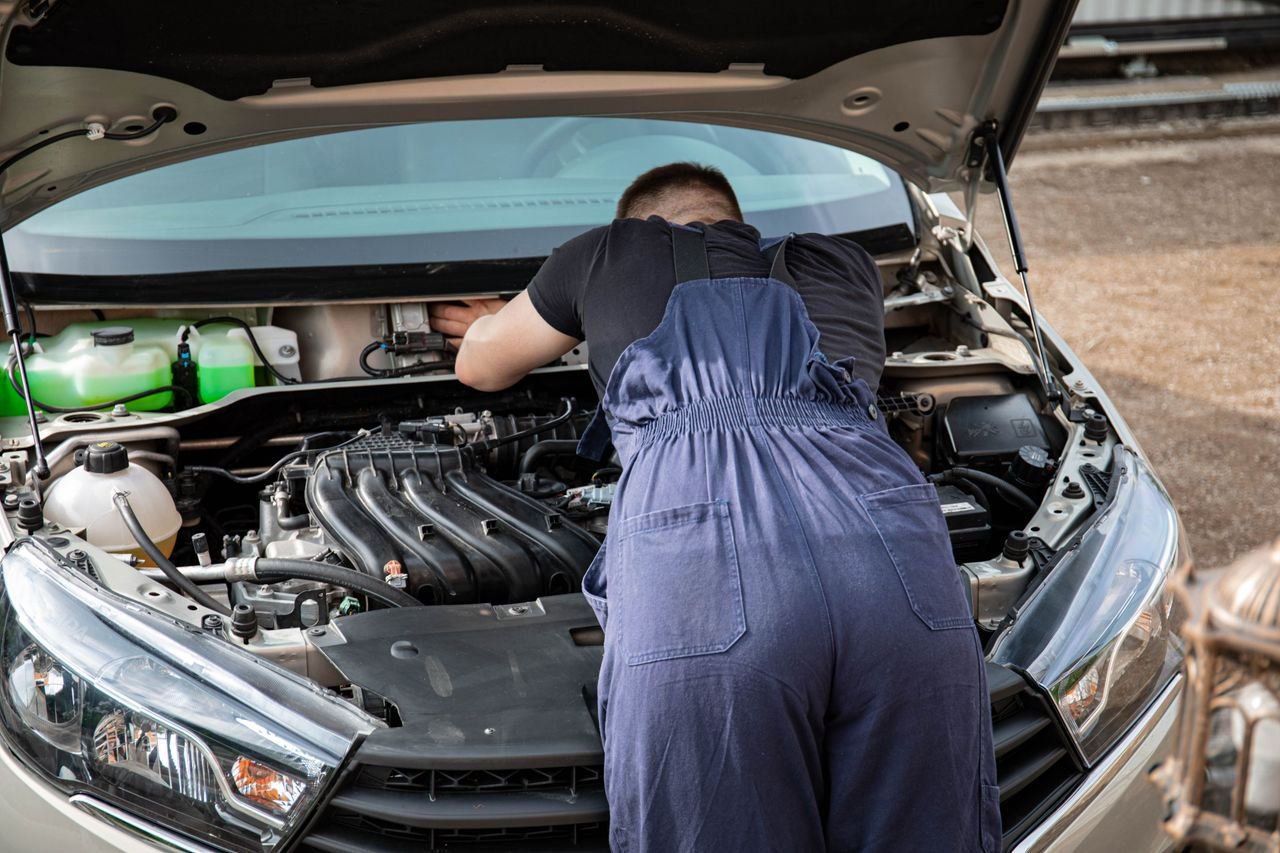 why-choose-us-02 An automotive mechanic performing engine maintenance on a car outdoors, showcasing mechanical skills.